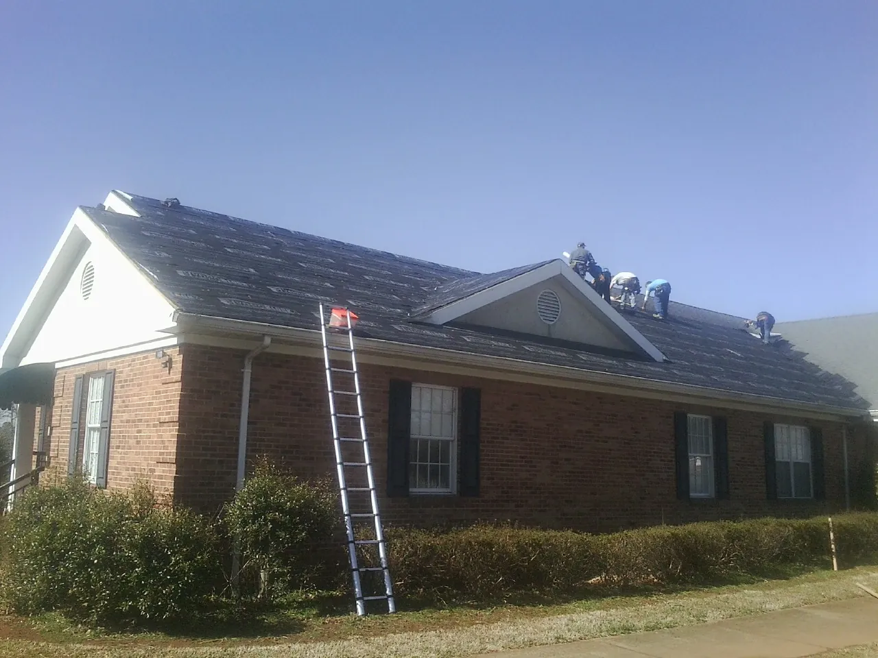 Crew tearing shingles off a brick ranch roof with a ladder set — Metal Roof Repair work by our crew in Deerfield