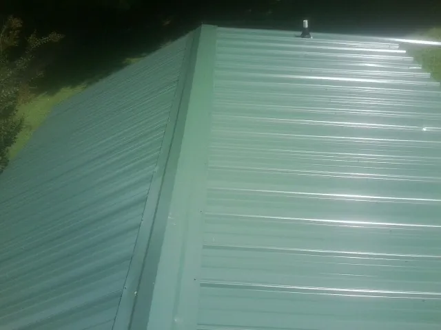 New green metal panels meeting at the ridge of a roof — Flat Roof Repair work by our crew in Deerfield